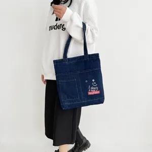 Detail of blue denim tote bag with front pocket and casual smiley face graphic design