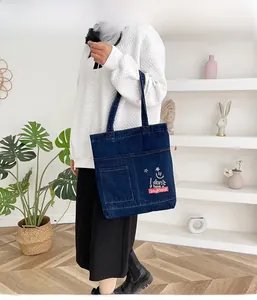 Dettaglio della borsa tote in denim blu con tasca frontale e grafica con faccina