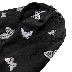 Detail of black distressed knit fabric with silver butterfly patterns and fringe texture