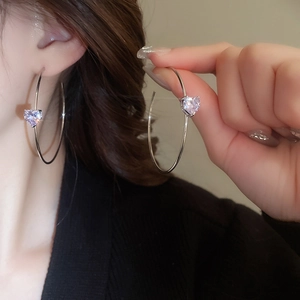 Détail de créoles en C argentées avec un grand zircon violet taillé en cœur