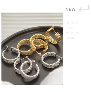 Macro shot of gold and silver woven texture hoop earrings on a black tray