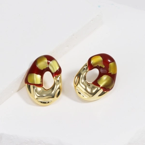 Macro shot of red enamel earrings with gold flecks on a textured stone surface