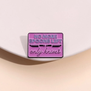 Détail d'un pin's en émail rose avec couteaux noirs et citation NO MORE SPOONS LEFT