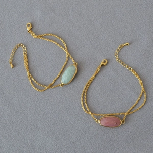 Dettaglio di bracciali a doppia catena dorata con ciondoli in pietra ovale