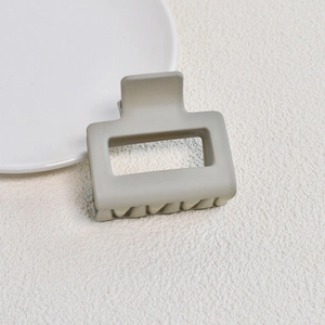 Detail of matte beige square claw clip on a white ceramic plate with a minimalist design