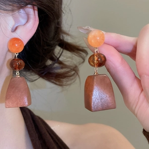 Detail of vintage geometric wood pendant earrings with orange beads on a model