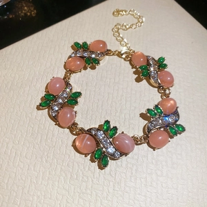 Close-up of golden bracelet with pink oval resin, green leaf gems and sparkling crystals