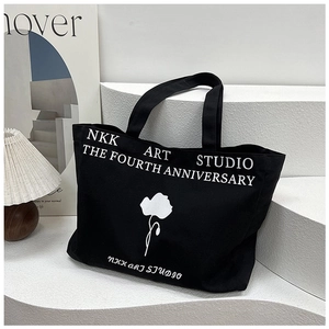 Close-up of a large black canvas tote bag with a white flower and artistic typography