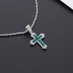 Gros plan détaillé du pendentif croix argenté orné de zircon vert et cristaux blancs
