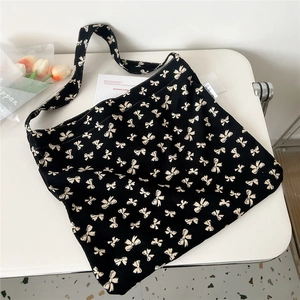 Detail of black canvas crossbody bag featuring dense white bow prints and wide strap