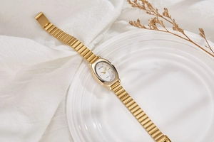 Detail of elegant gold oval quartz watch resting on white ceramic with dry flowers
