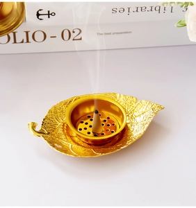 Close-up of golden leaf-shaped incense burner with burning cone on a white desk