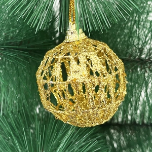 Macro detail of a golden hollow Christmas tree ornament ball with glitter on a green branch