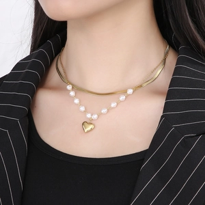 Detail of layered gold snake chain and pearl necklace with heart pendant on model