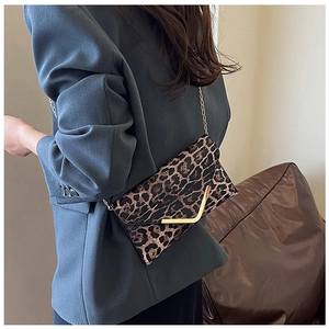 Detail of leopard print crossbody bag featuring gold V-shaped buckle and fine chain strap