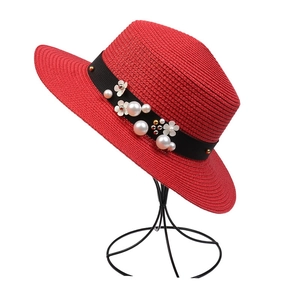 Macro shot of red woven straw hat with pearl floral trim on a black ribbon detail