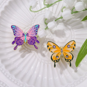 Colorful alloy butterfly enamel pins in purple and orange on a ceramic plate