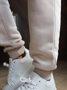 Detail of ribbed cuffs on beige jogger pants paired with white sneakers on wood floor