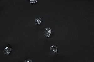 Détail macro de perles en cristal cousues sur une robe moulante noire dos nu en maille