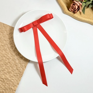 Detail of red ribbon bow hair clip with long streamers on a decorative white plate
