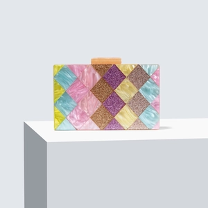 Colorful acrylic clutch bag with geometric diamond patchwork and gold clasp on a pedestal