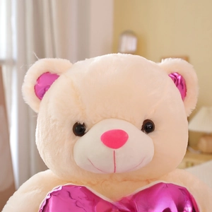 Close-up of soft beige teddy bear plush with metallic pink heart details and fine fur texture