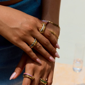 Close-up of stacked gold rings with colorful zircons and a MAMA letter bracelet
