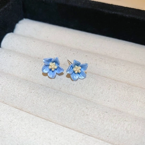 Dettaglio di orecchini a lobo con fiori blu e petali lucidi in un portagioie in velluto
