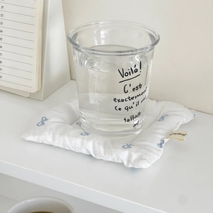 Close-up of white quilted coaster with blue bow prints and minimalist glass cup