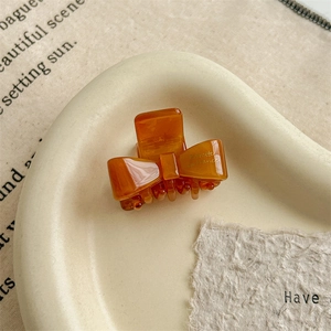 Detailed shot of an amber acetate bow hair claw clip with gold lettering on a ceramic plate