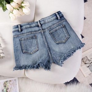Dettaglio di shorts in denim blu con orli sfrangiati, accessori moda e rose bianche su sfondo