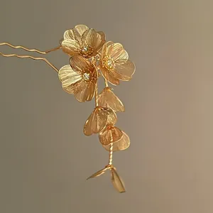 Détail d'un pic à cheveux en métal doré avec fleurs ciselées et pompons scintillants