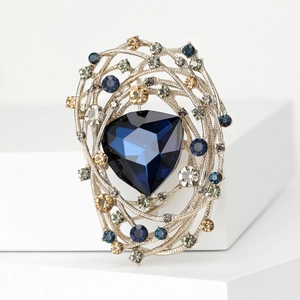 Detailed macro of a silver-toned bird nest brooch with a large blue faceted crystal center