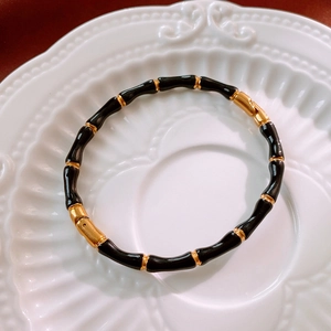 Dettaglio macro del bracciale a motivo bambù nero e oro su un piatto di ceramica