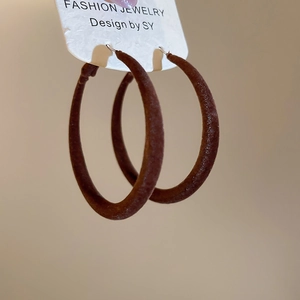 Détail macro de grandes boucles d'oreilles ovales avec finition floquée marron foncé et tiges en argent