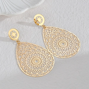 Macro shot of gold teardrop earrings with intricate mandala filigree patterns on ceramic tray