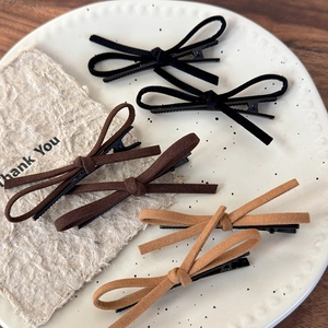Set of six suede bow hair clips in black, dark brown, and light brown on a ceramic tray