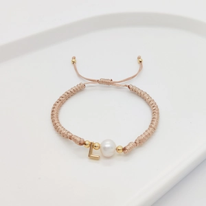 Macro detail of hand-woven cord bracelet featuring a natural pearl and golden letter L charm