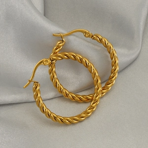 Detailed close-up of golden twisted hoop earrings on soft silk fabric background