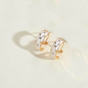 Close-up of gold-plated hoop earrings with white enamel honeycomb pattern detail