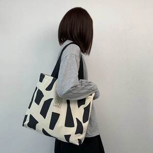 Detail of a large cream canvas tote bag with black geometric patterns and logo tag