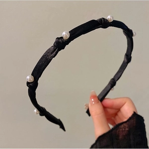 Close-up of black pleated fabric headband with elegant white pearl embellishments