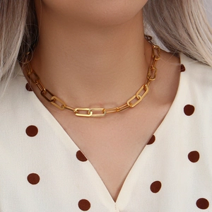 Close-up of a model wearing a golden paperclip link necklace on a white polka dot shirt