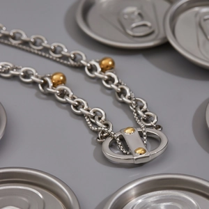 Détail d'une chaîne en acier titane argenté avec billes dorées et pendentif à rivets