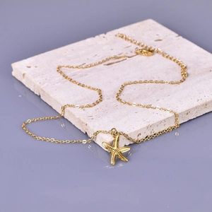 Detail view of gold starfish pendant necklace on textured white stone surface