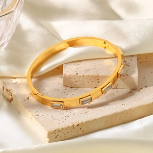 Détail d'un bracelet en titane doré avec zircons rectangulaires sur soie beige