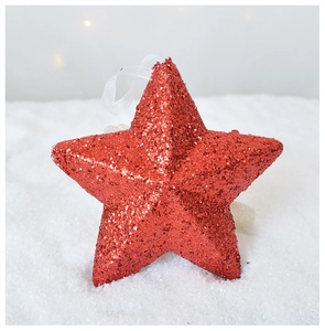 Close-up of sparkling red star Christmas ornament on soft white snowy background