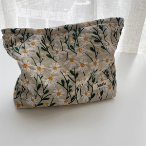 Detail of embroidered daisy flowers on a beige cotton linen zipper cosmetic bag