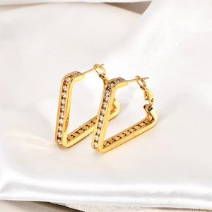 Detail of 18K gold-plated V-shaped hoop earrings with clear crystals on white satin