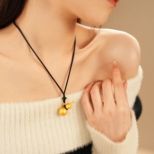 Detailed close-up of a brushed gold gourd pendant on a black cord worn by a model